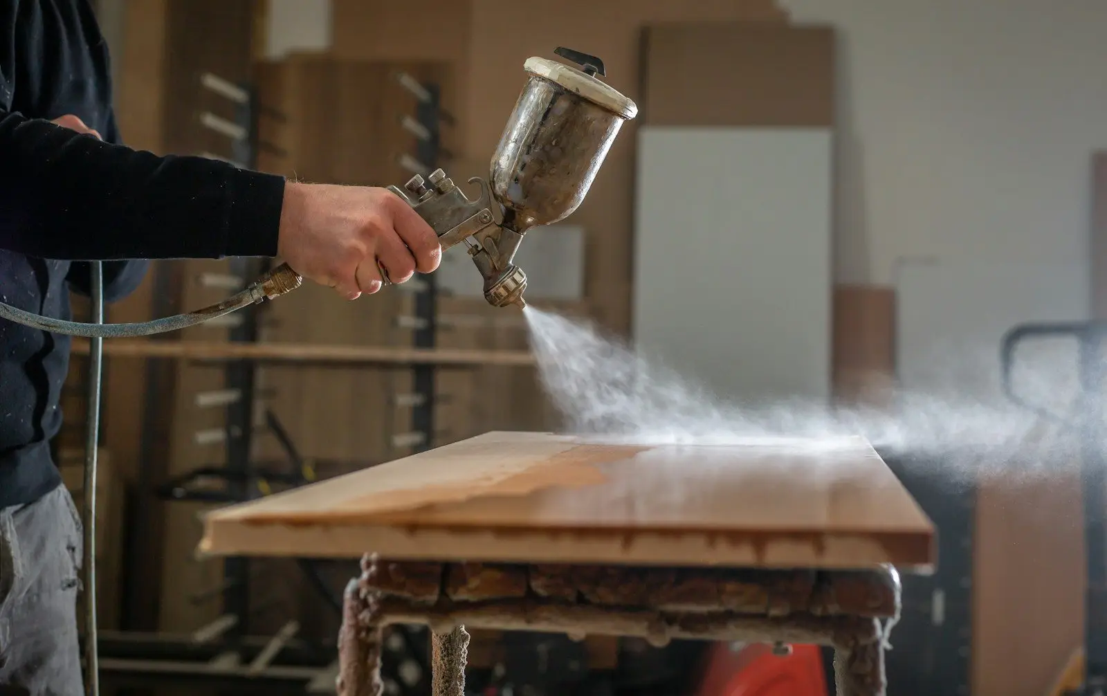 Mit der Spritzpistole wird Lack auf eine Holzplatte aufgetragen