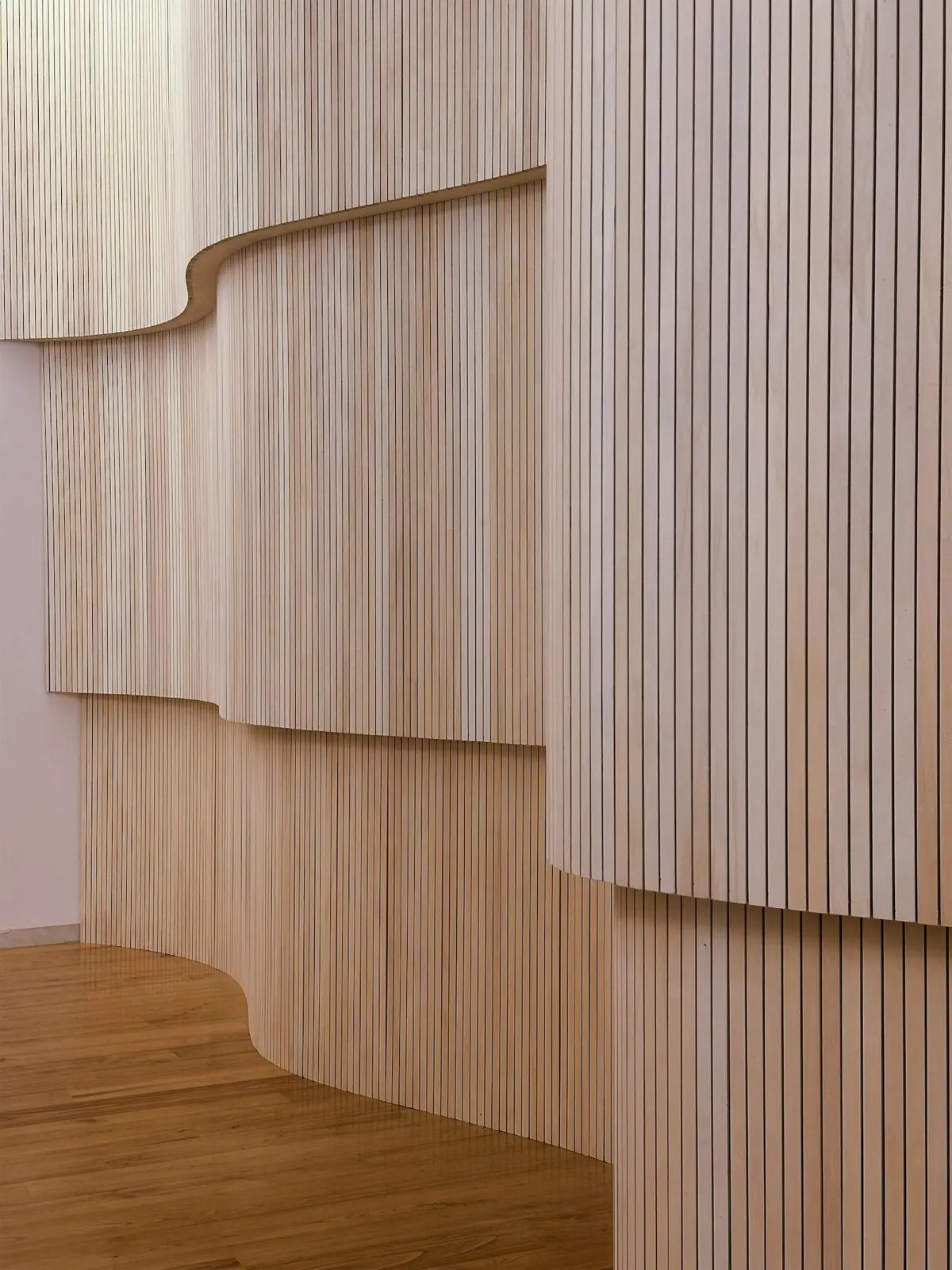 Geschwungene Wand aus hellen, senkrechten Holzlamellen über einem Eichenboden