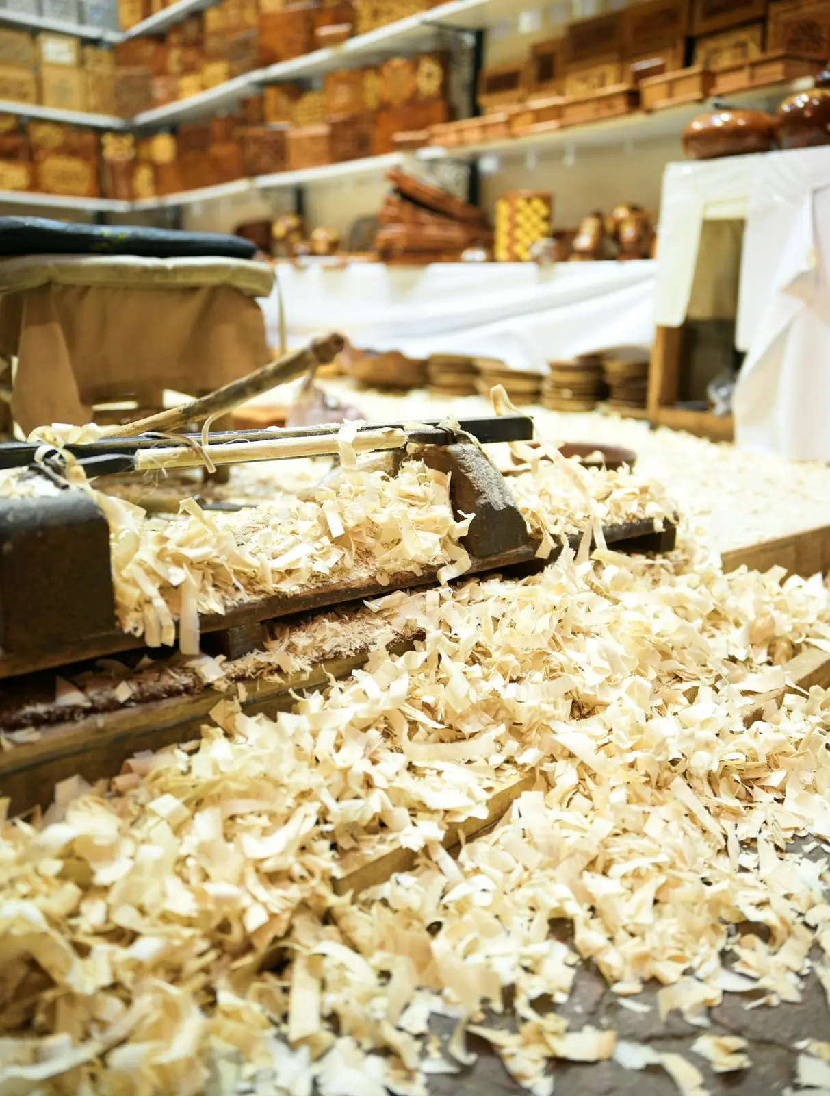 Hobelspäne auf einer Werkbank, dahinter Regale mit Holzteilen
